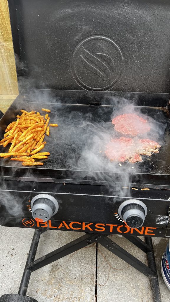 Smashburgers and fries cooking on a flat top grill